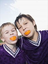 Portrait of boys in soccer uniforms with orange wedges in mouth. Date : 2008