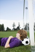 Boy laying on soccer ball against goal. Date: 2008