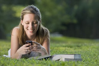 College student reading in grass and text messaging. Date: 2008