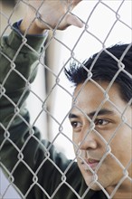 Close up of young man leaning against chain-link fence. Date : 2008