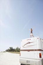 Woman standing on motor home with arms outstretched. Date: 2008