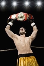 Boxer holding championship belt overhead in boxing ring. Date: 2008