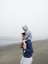 Father carrying son on shoulders on beach. Date : 2008