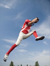 Football player in mid-air holding football. Date: 2008