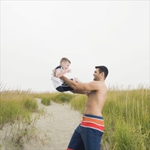 Father lifting son on beach. Date: 2008
