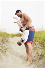 Father holding son upside down on beach. Date: 2008
