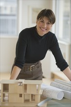 Portrait of architect leaning on table with building model and blueprints.