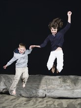 Brother and sister jumping off driftwood. Date: 2008