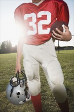 Football player holding helmet and football on field. Date: 2008