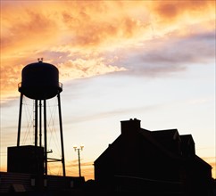 Water tower and house against sunset sky. Date: 2008