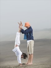 Mother holding daughter upside down on beach. Date: 2008