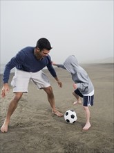 Father and son playing soccer on beach. Date: 2008