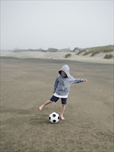 Boy kicking soccer ball on beach. Date: 2008