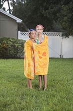 Portrait of sisters wrapped in towel standing in backyard. Date : 2008
