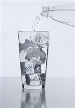 Water from bottle pouring into glass with ice cubes.