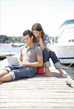 Couple using laptop on dock. Date : 2008