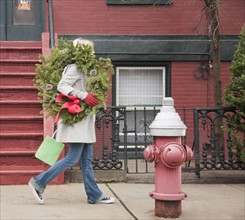 Woman carrying Christmas wreath on urban street. Photographe : Jamie Grill