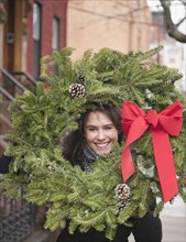 Woman carrying Christmas wreath on urban street. Photographe : Jamie Grill