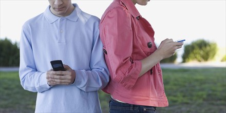 Young couple text messaging outdoors. Photographe : PT Images