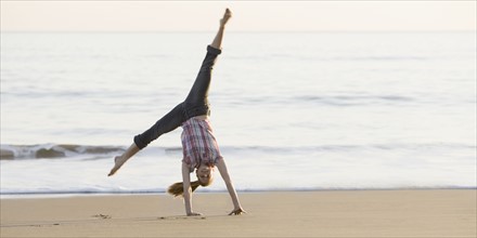 Woman doing cartwheel on beach. Photographe : PT Images