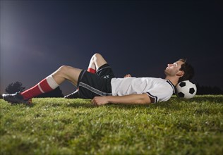 Soccer player resting on ball.
