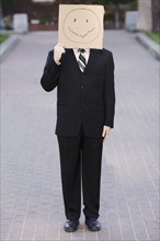 Businessman holding cardboard smiley face. Photographe : PT Images