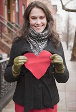 Woman holding heart cutout on urban street. Photographe : Jamie Grill