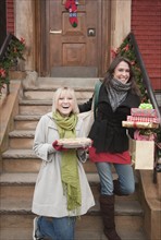 Women carrying Christmas gifts on front stoop. Photographe : Jamie Grill