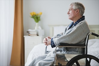 Senior man in wheelchair looking out window.