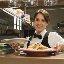 Waitress taking plates of food from kitchen.