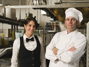 Chef and waitress posing in restaurant kitchen.