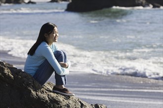Teenage girl sitting on coastal rock. Photographe : PT Images