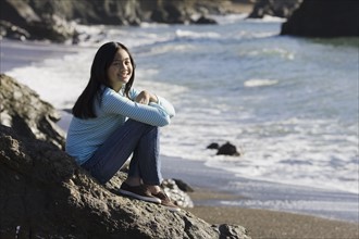 Teenage girl sitting on coastal rock. Photographe : PT Images