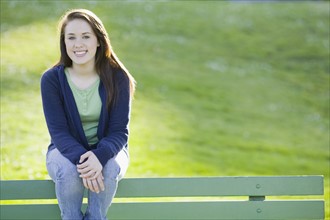 Teenage girl sitting on park bench. Photographe : PT Images