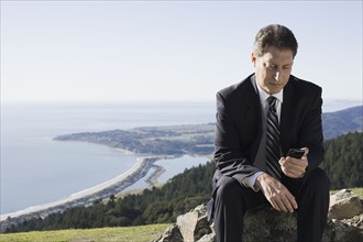 Businessman text messaging on remote hill. Photographe : PT Images