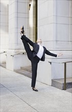 Businesswoman stretching on urban sidewalk. Photographe : PT Images
