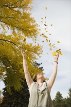 Woman throwing autumn leaves in air.