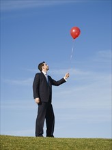 Businessman holding red balloon.