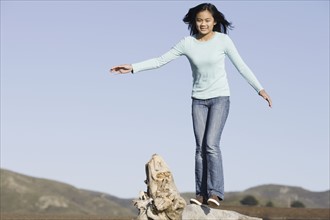 Teenage girl balancing on driftwood. Photographe : PT Images