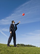 Businessman letting red balloon go.