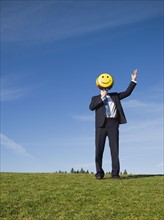 Businessman holding smiley face balloon over face.