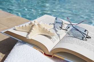 Book and sunglasses by swimming pool.