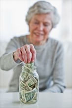 Senior woman putting banknote into money jar.