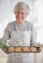 Senior woman holding tray with baked cookies.