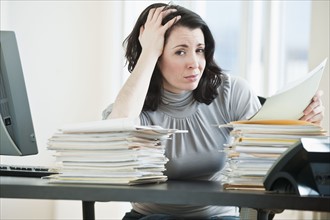 Stressed business woman holding paperwork in office.