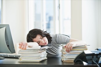 Business woman sleeping on paperwork at desk in office.