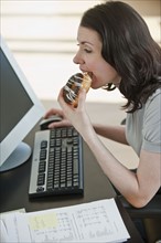 Business woman eating donut at desk in office.