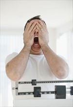 Mature man on scales screaming and covering his eyes.