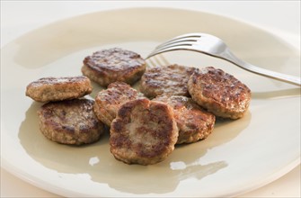 Fried slices of sausage and fork on plate.