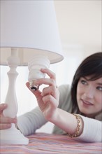 Young woman changing light bulb. Photographe : Jamie Grill